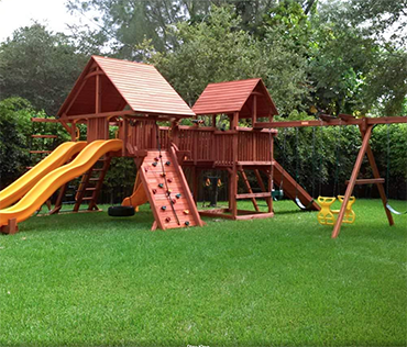 A large Woodplay playset in Coral Springs, Florida, with rock wall, two slides, swingset and wood roofs.